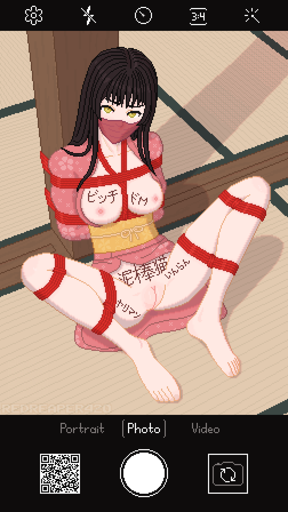 Pixel art of a nude girl with black hair and yellow eyes in an open pink kimono bound with red shibari ropes, gagged, and sitting spread on a tatami mat. She has marker writings on her body. Phone camera interface frames the picture.