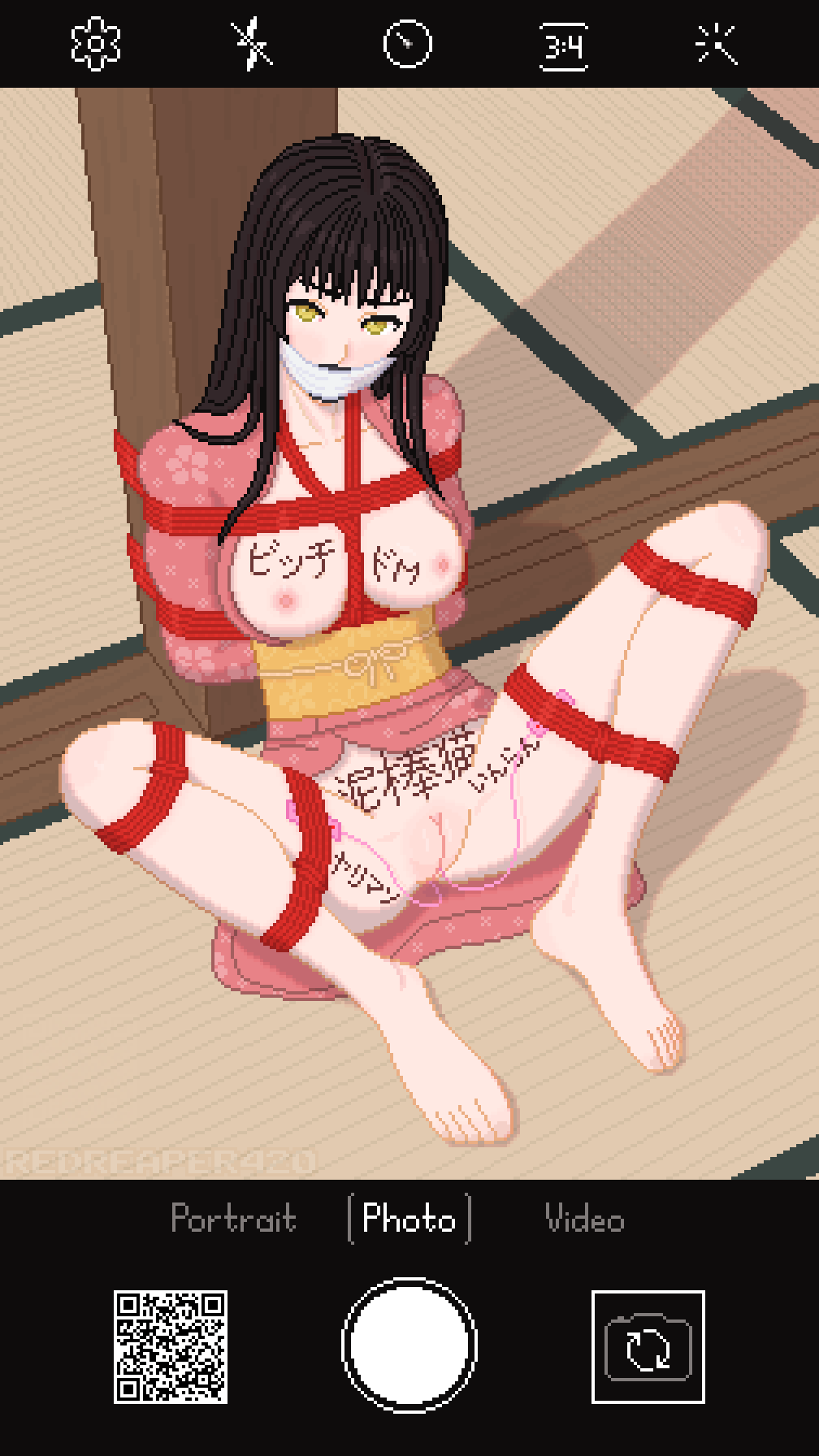Pixel art of a nude girl with black hair and yellow eyes in an open pink kimono bound with red shibari ropes, gagged, with vibrators attached, and sitting spread on a tatami mat. She has marker writings on her body. Phone camera interface frames the picture.